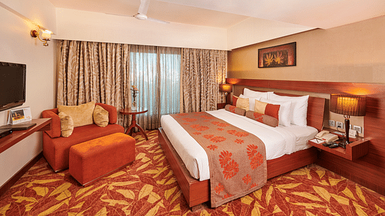 Room at Pride Hotel Nagpur featuring a plush bed with lamps on the both sides on nightstands and a TV mounted in front o the bed