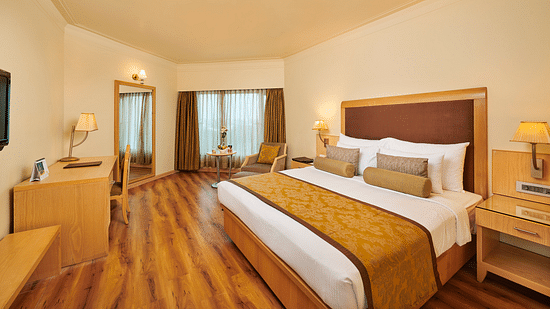 Image of a room at Pride Hotel Nagpur featuring a plush bed with cushioned wooden headboard with wooden nightstands on both sides