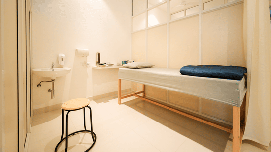 Single bed with folded blanket beside attached sink and stool in private room at The Residences at CSE.