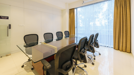 Conference table with seven office chairs near glass door and window with curtains at The Residences at CSE.
