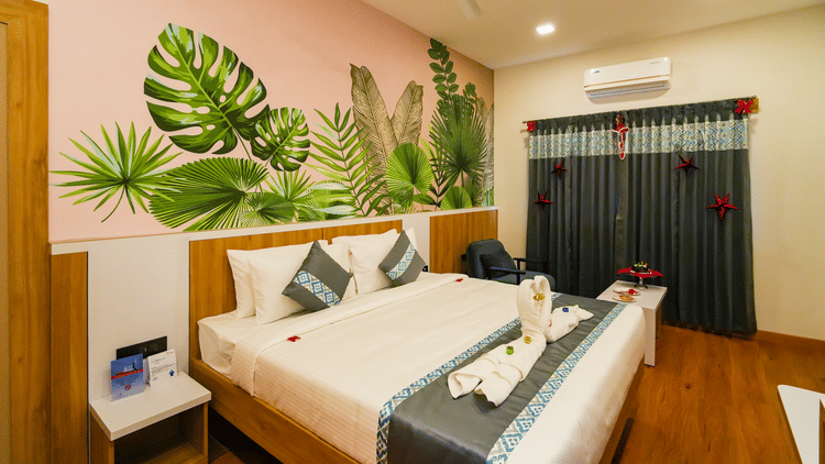 A view of the bedroom featuring a bed with a grey and white duvet, a tropical leaf mural, and a dark/red door in the background.