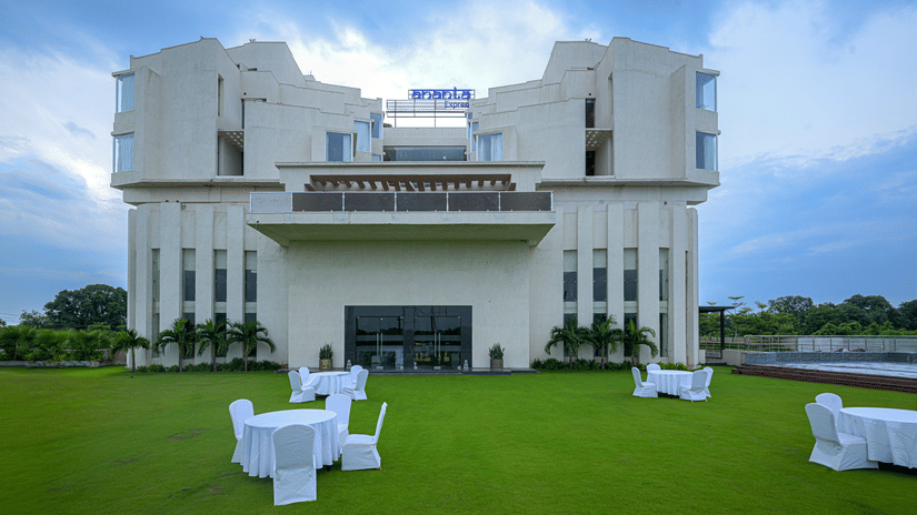 White hotel building set against a blue sky with a manicured lawn arranged with outdoor tables and chairs.