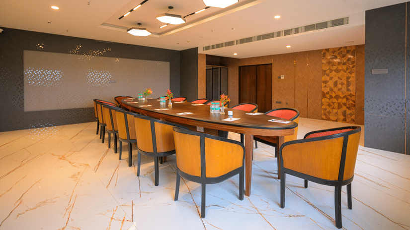 Meeting room arranged with a long conference table, orange chairs, presentation screen and patterned feature wall.