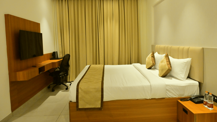 Deluxe room at Bhavanis Vista By Icon Hosur with a king bed, wooden work desk, and gold-toned curtains.