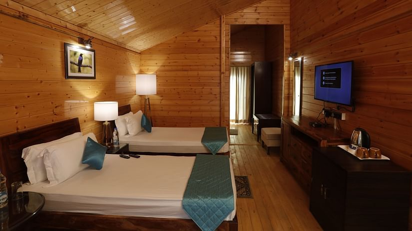 A spacious wooden cottage bedroom at Digantaa Resort in Mukteshwar a large bed, TV, and warm lighting, creating a cosy ambience