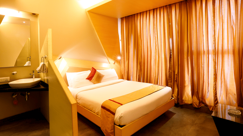 Cosy attic-style bedroom at Dragonfly Hotels with a sloped ceiling, double bed, warm lighting, and large curtained windows.