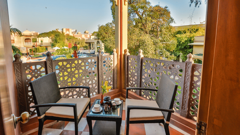 Spacious balcony at the Heritage Village Resort & Spa, Manesar,  facilitated with a coffee table and two chairs looking over the rest of the property against a bright blue sky.