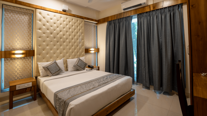 A bedroom at one of the service apartments of Home2 India featuring a plush bed next to a curtained window under warm lighting