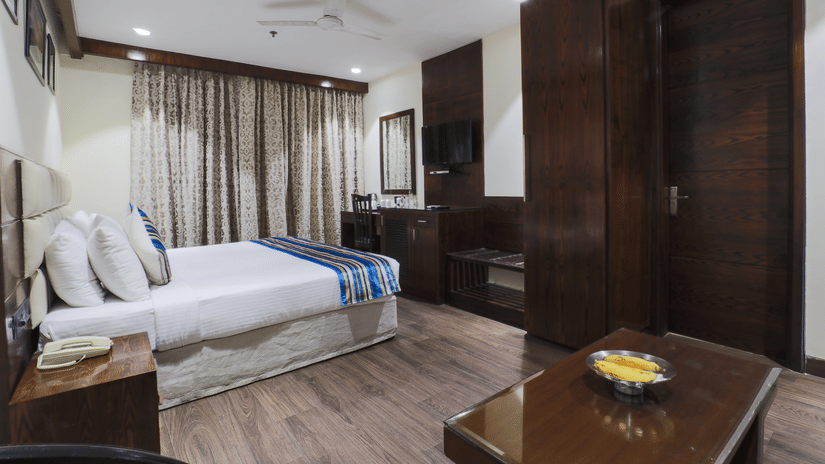 Spacious room with modern interiors, cozy bedding, and elegant wooden furnishings at Hotel Bluestone (Nehru Place) by The Cosy Hotels.