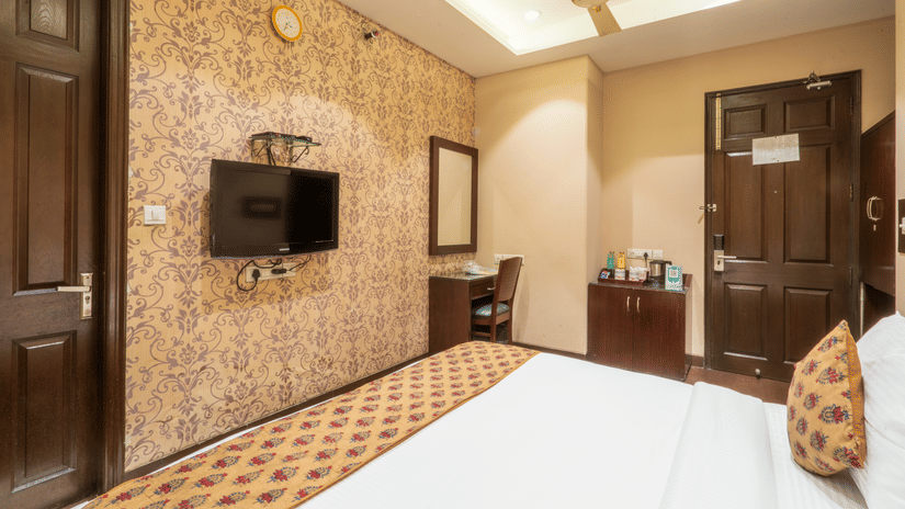 Comfortable room with stylish décor, wall-mounted TV, and essential amenities at Hotel Bluestone (Nehru Place) by The Cosy Hotels.