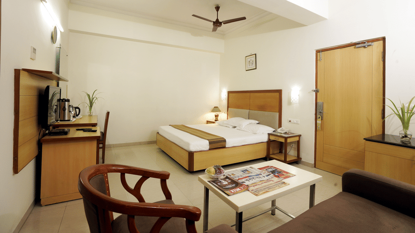 Suite room with a comfortable bed, seating area, table and wooden furnishings at Hotel Geetha Regency, Guntur.