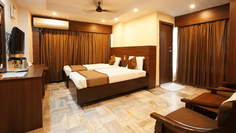 Deluxe room interior with a comfortable bed, wooden furnishings and warm lighting at Hotel Jaya Residency, Kakinada.