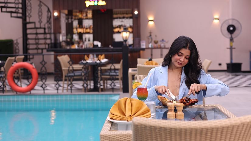 A woman feasting on food at her table next to the swimming pool at Skygrill restaurant with the bar counter in the background