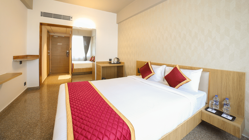 A double bed, a wooden door, and a wall mirror at Icon Express By Bhagini, Mahadevapura.