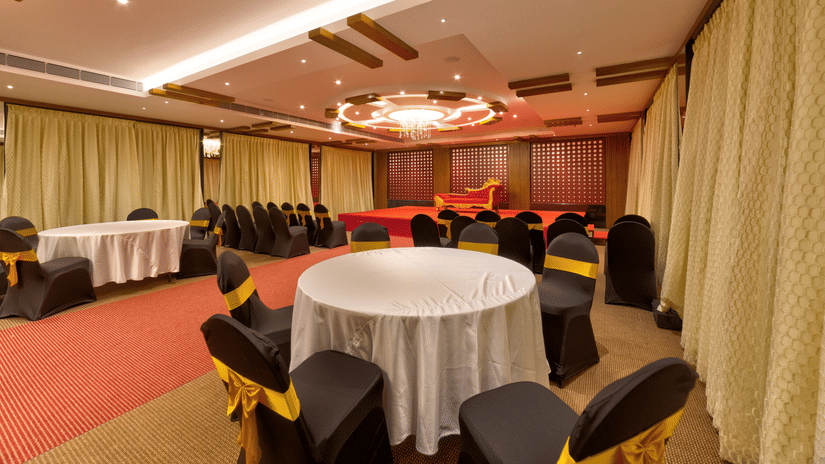 Round tables, black and gold chairs, a red carpet, and a stage setup inside the banquet hall of Icon Express By Bhagini, Hoodi.