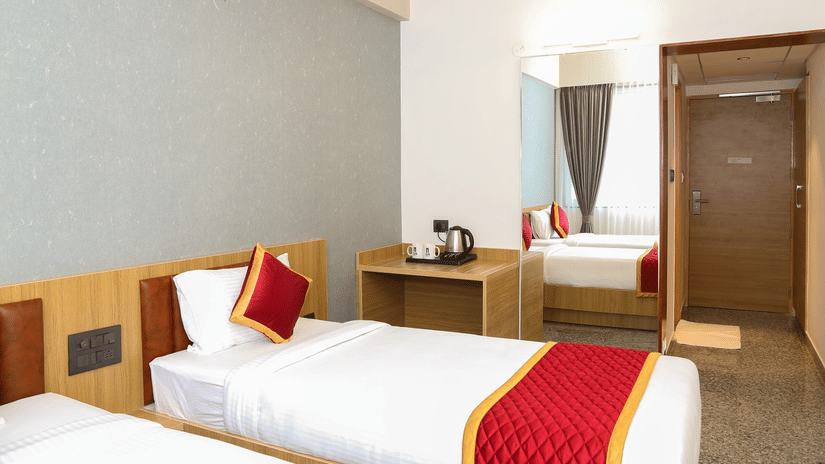 Two single beds, a wooden desk, and a large mirror at Icon Express By Bhagini, Mahadevapura.