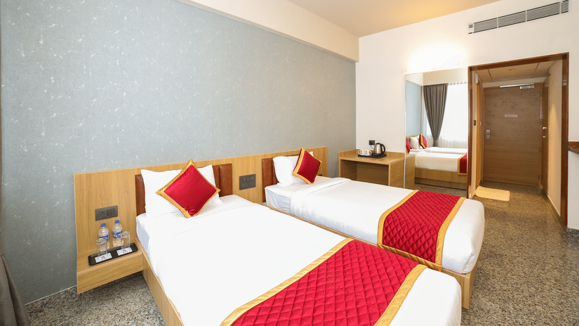 Two single beds with red runners, white linens, and a central bedside table at Icon Express By Bhagini, Mahadevapura.