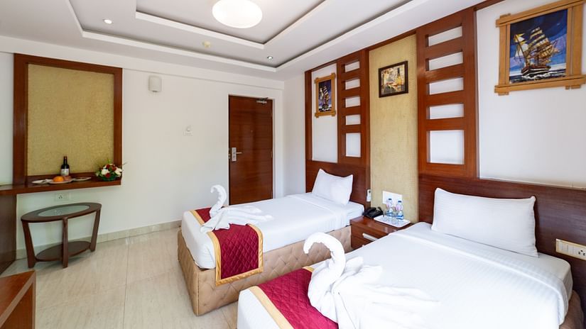 Symmetrically designed Deluxe Twin Room with a soft false ceiling light, decorative wall panels, and plush bedding—ideal for dual occupancy with ample walking space.