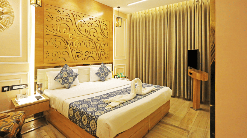The Deluxe Room of JRD Luxury Business Hotel showcasing a double bed, wooden flooring, a television,  and ceiling lights.
