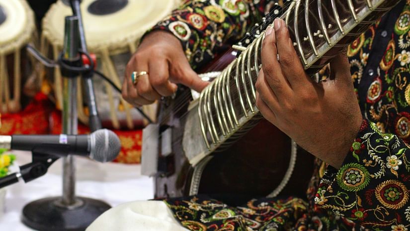 A classical music artist holding a sitar in his hand 