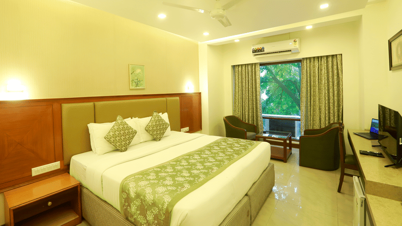 The Deluxe Room at Kohinoor Executive featuring a double bed, seating area, and warm lighting.