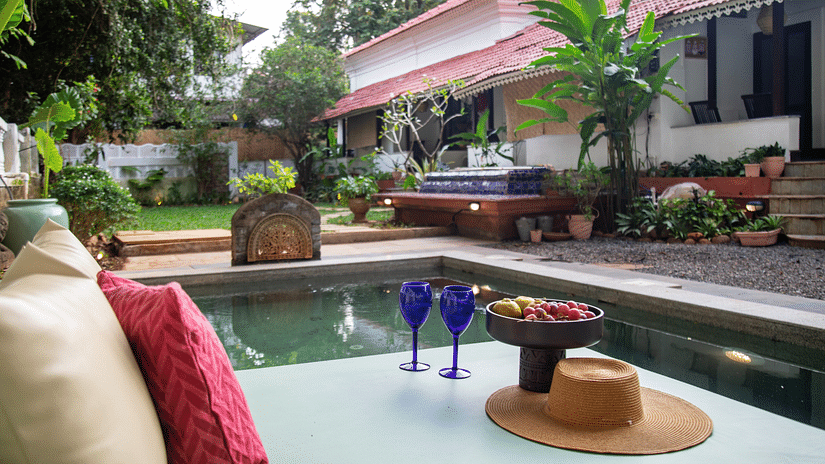 L shaped pool side with two blue wine glasses and surrounded by greenery @ Lamrin Ucassaim Hotel, Goa
