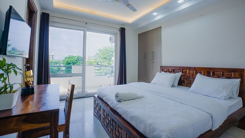 An image of a bedroom featuring a king size bed, a flat TV screen, a work desk and chair, and some flower pots - Lime Tree Hotels on Golf Course Extension Road Gurgaon