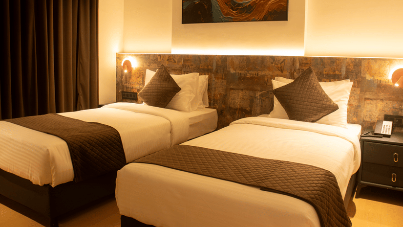 2 single beds room with bedside lamps, headboard panel, and wall art at Magnus Lxia Premier, Kalyani Nagar.