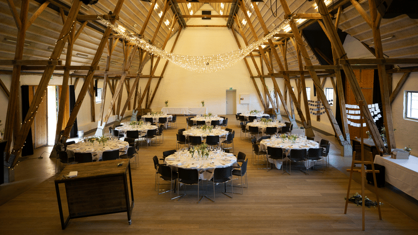 Interior of a large reception hall with high-pitched wooden-beam ceilings and formal dining setups.