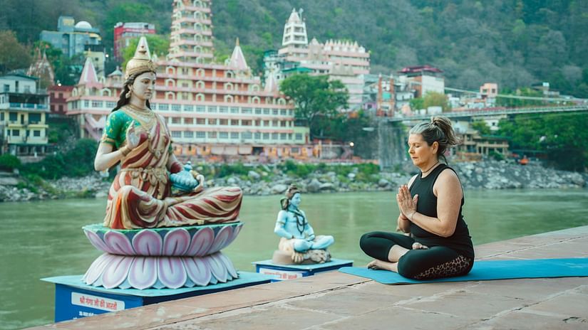 elderly woman meditating in front of a statue of Parvati on the Ganges