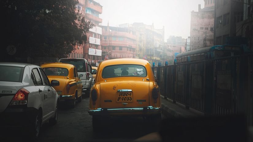 a yellow taxi driving through the traffic of Kolkata