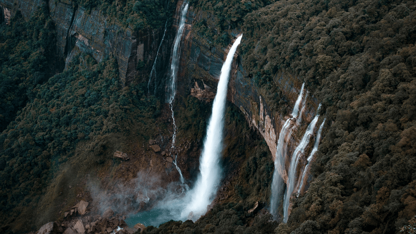 Aerial view of Nohkalikai Falls plunging from a forested clifftop into a turquoise plunge pool surrounded by deep green Khasi mountainsides.