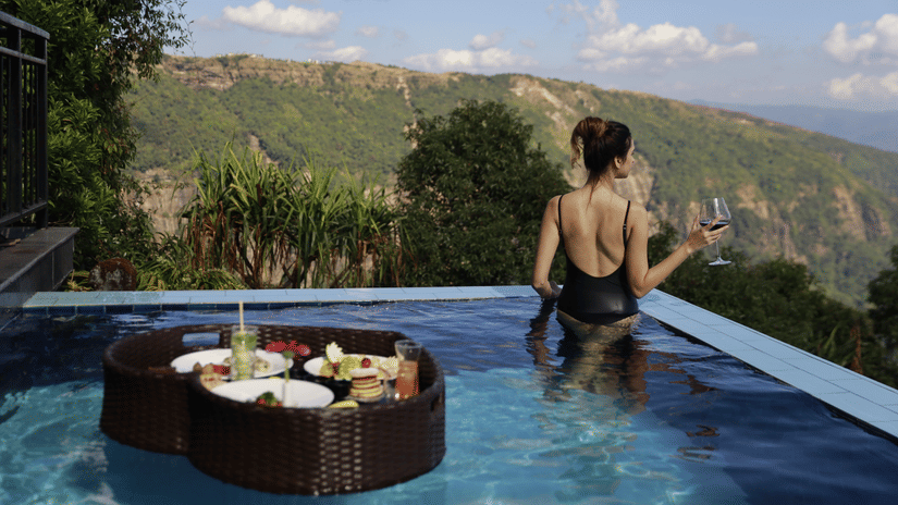 Woman in private plunge pool at Polo Resort Cherrapunji with floating breakfast tray and wine glass overlooking the green Khasi Hills valley.