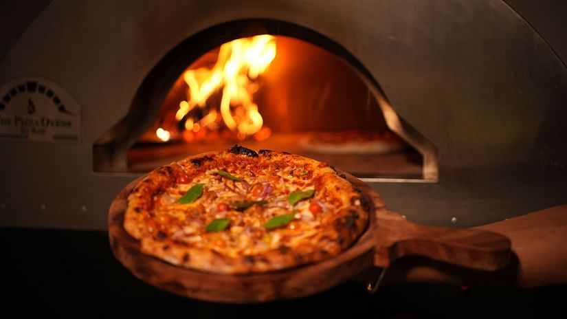 Close up of a wood fire pizza near a wood fire oven featuring it's delicious loaded cheese and veggies at Rangamati Garden Resort.