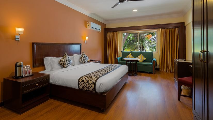 An image of a bedroom with king size bed with bedside tables, lamps, cabinets. and an open window - Ras by Treat Resorts