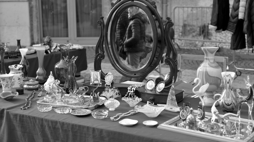 An outdoor market table filled with glass bottles, a round mirror, and various antique trinkets.