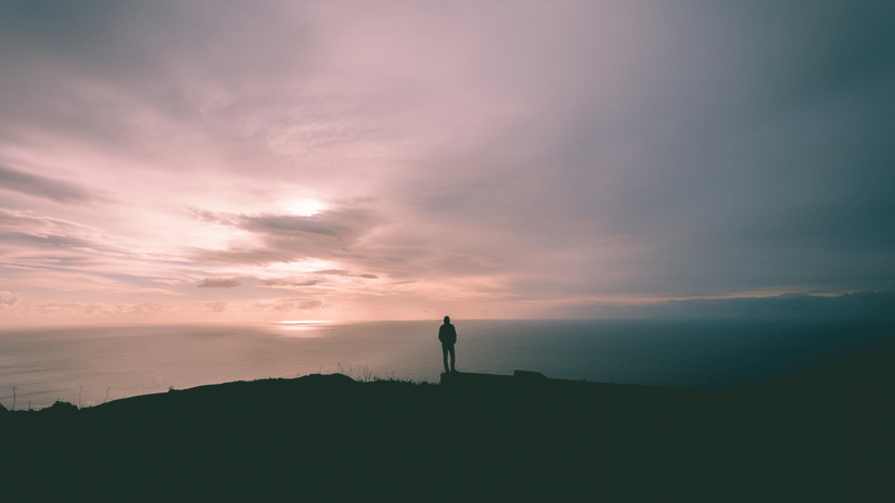 A person standing on top of a mountain looking at the sun set in the distance