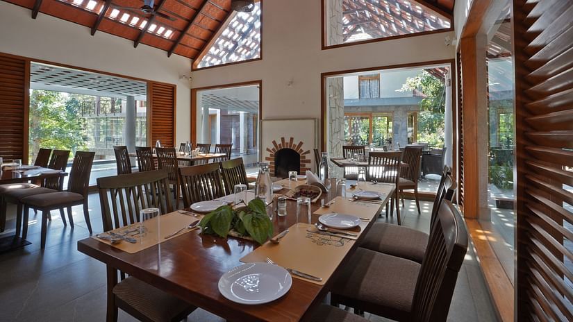 An image of a restaurant featuring chairs and tables where flower vase, plates, table mats, and cutlery are placed - The Birchwood Retreat