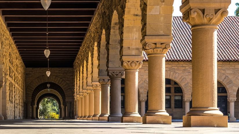 A sunlit colonnade with repeating arches and columns, leading to a shadowed archway in the distance.