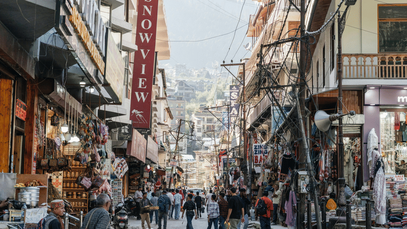 A bustling, narrow commercial street lined with tall buildings and signs, leading up a hill in a town.