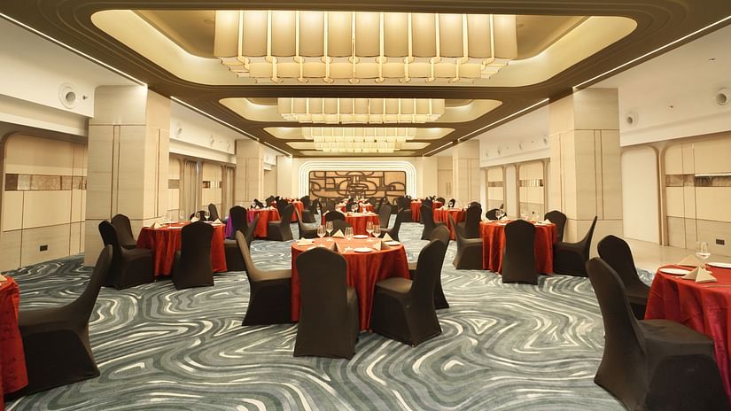 Event hall with round tables draped in red, surrounded by black chairs. Neutral walls and patterned flooring - The Orchid Hotel, Chandigarh