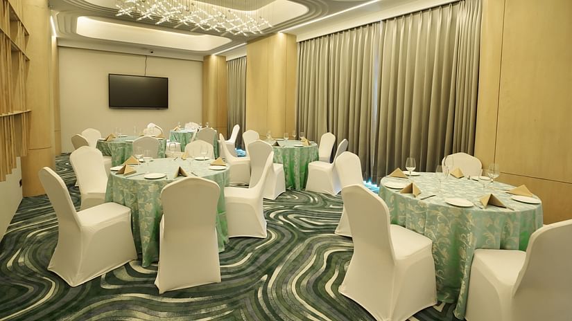 Dining area with round tables draped in light green, surrounded by white chairs. Patterned carpet and soft lighting - The Orchid Hotel, Chandigarh