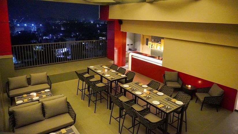 The rooftop of Skydip pool deck and bar at night, showing tables and chairs under a lit trellis, with a vibrant cityscape visible in the background - The Orchid Hotel, Chandigarh