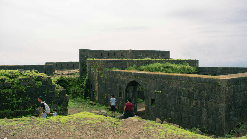 A far-out view of a fort that is being consumed by greenery with people also in view.