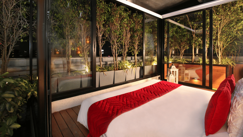 A bedroom at Theory9 - Premium Service Apartments, Bandra with a large bed and floor-to-ceiling windows overlooking a night-time rooftop garden with trees