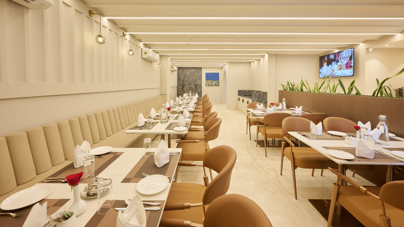 A restaurant dining room at Tulip Inn Gurugram with long rows of set tables, chairs, and a linear light-panelled ceiling.