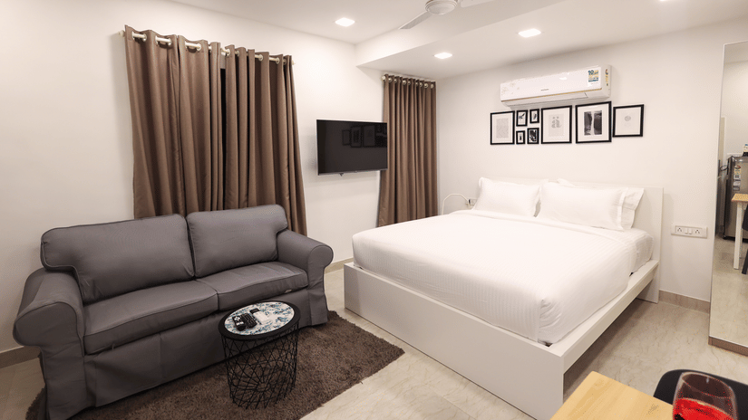 A spacious room featuring a large bed, a 2-seater sofa, a wall-mounted TV, and an A/C unit at Wabi - Sabi by Alamiko, Juhu. 