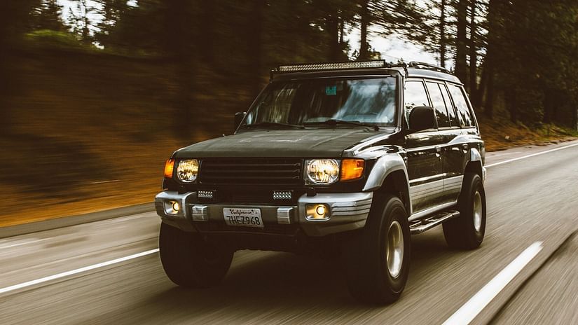 Green SUV driving on a winding road through a forest.