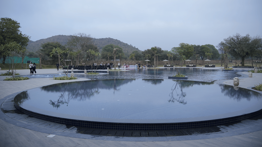 Circular water feature surrounded by trees and pathways, with hills visible in the background under a cloudy sky at Ananta Spa and Resort, Ajabgarh