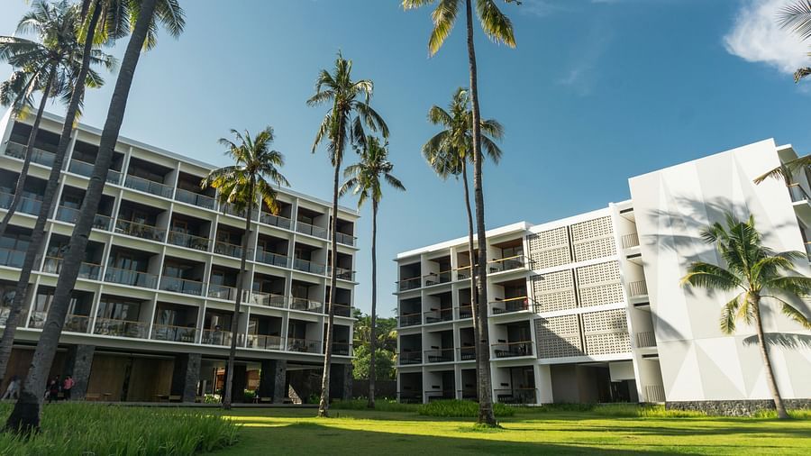 A modern building complex with palm trees under a blue sky.